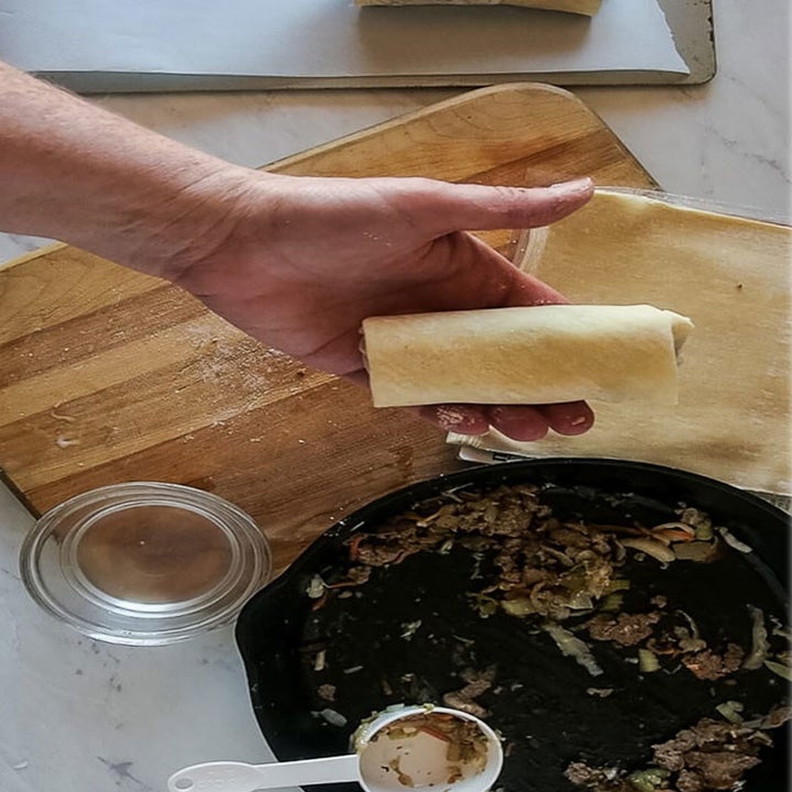 Someone rolling egg roll mixture from a skillet into a wrapper.