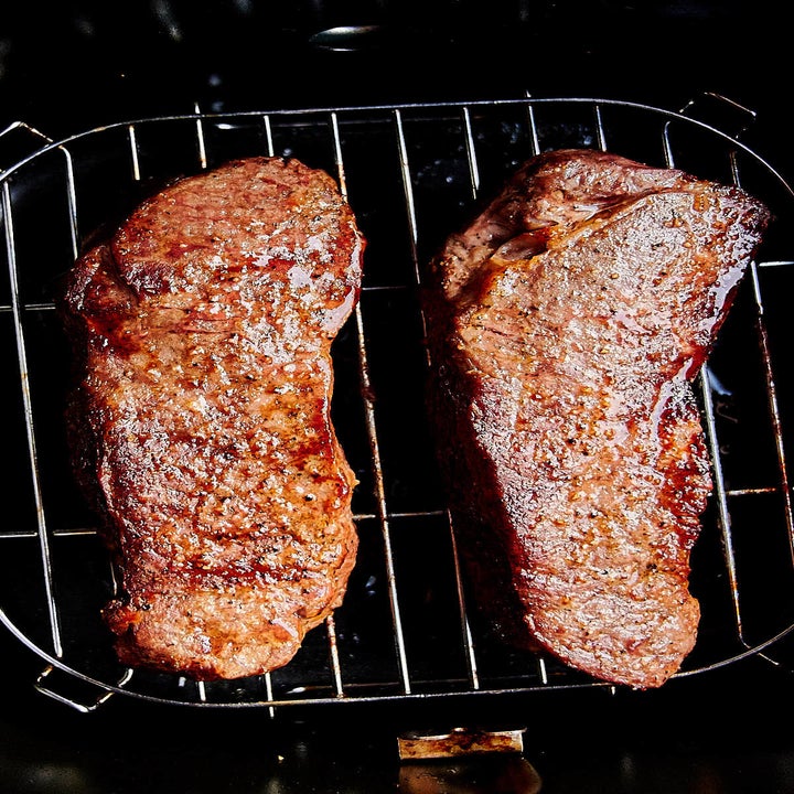 Two cooked steaks with crispy exteriors in an air fryer.