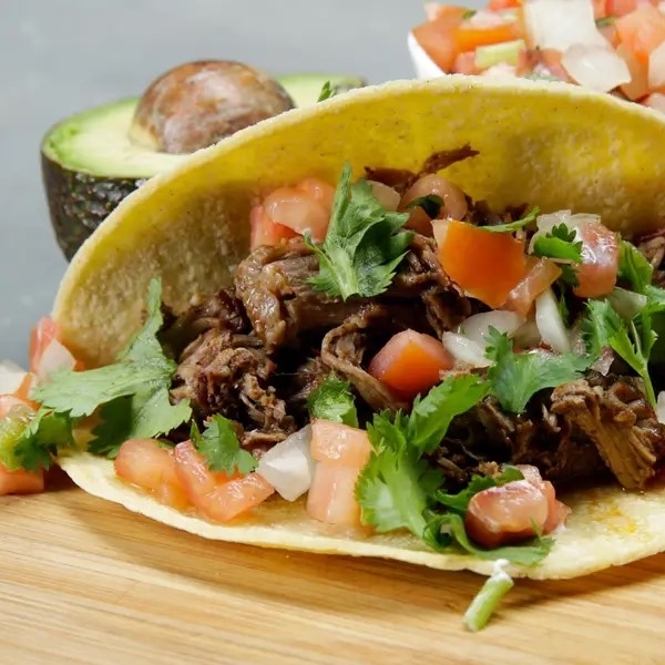 A taco filled with beef, fresh cilantro, diced tomatoes, and onions on a wooden surface