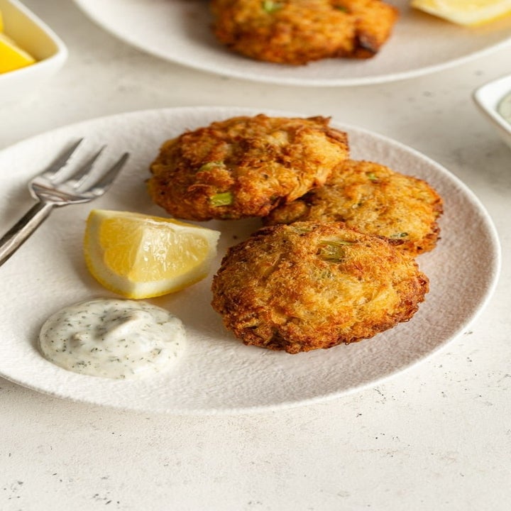 Three crab cakes on a plate with tartar sauce and lemon.